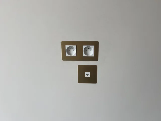 Double prise électrique et prise réseau de finition bronze sur un mur clair